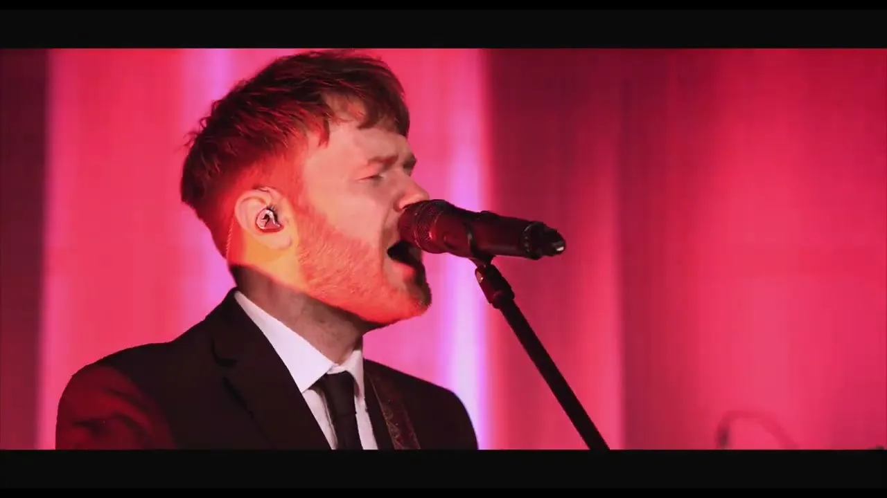 Man in suit singing into a microphone against a pink and red lit background.