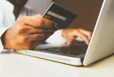 Person holding a credit card and typing on a laptop keyboard.