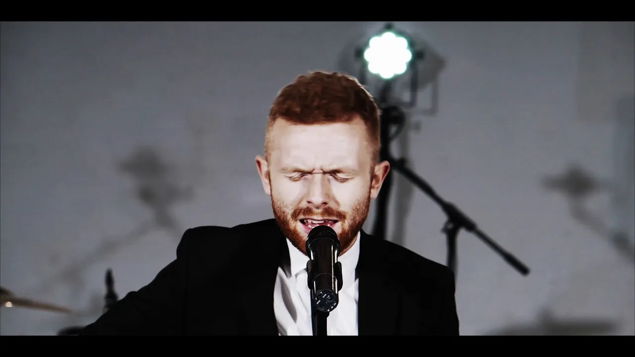 Man with red hair and beard singing passionately into a microphone in a studio setting.