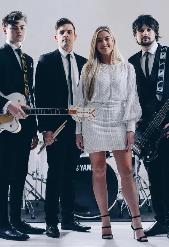 Four musicians in formal attire posing with instruments in front of a drum set.